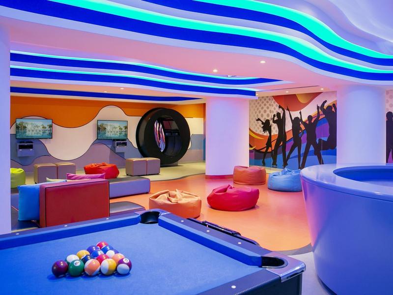 Moderner Spiel- und Sitzbereich mit Billardtisch, bunten Sitzkissen und blau beleuchtetem Deckendekor.