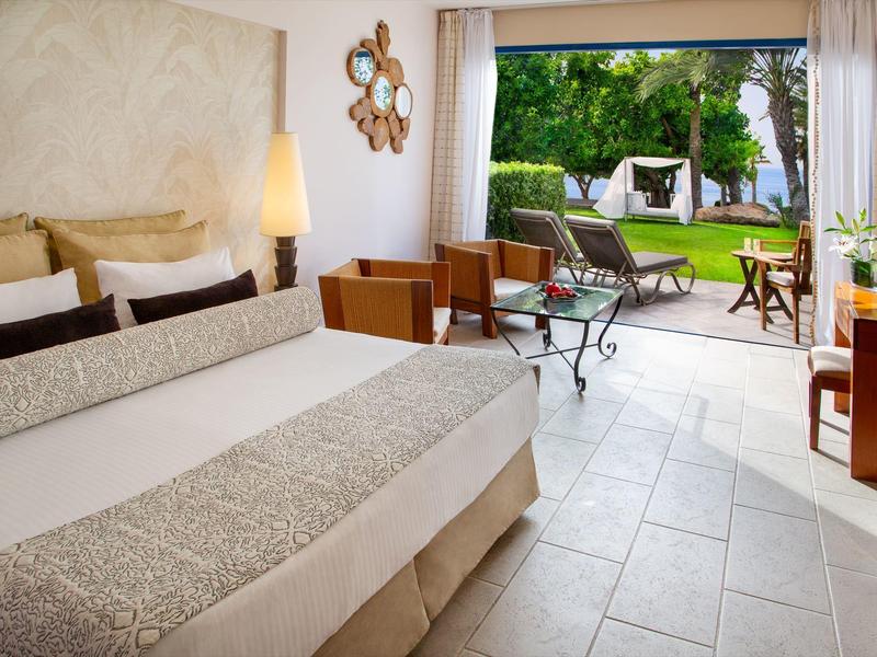 Hotelzimmer mit großem Bett und Zugang zum Garten mit Sitzbereich und Liegestühlen.