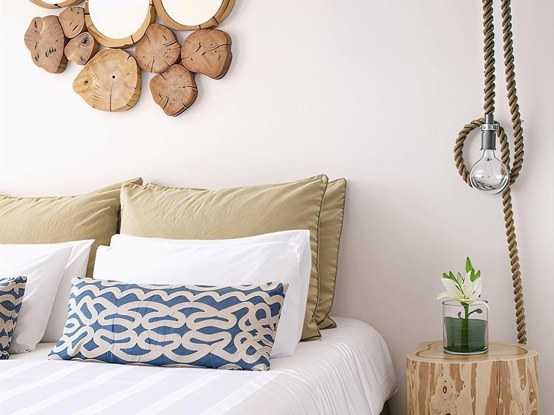 Schlafzimmer mit weißem Bett, dekorativen Holzwandspiegeln und kleinem Holztisch mit Pflanze.