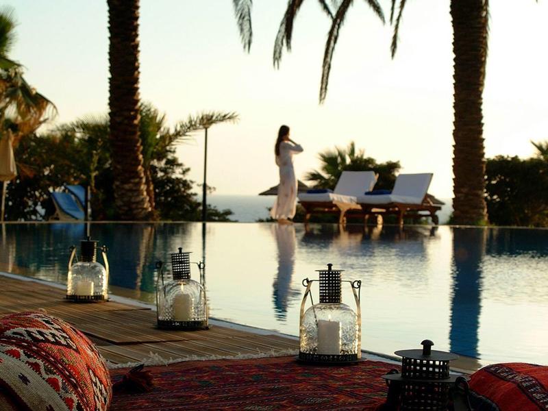 Sonnenuntergang an einem Pool mit Palmen, Liegen und Kerzen für eine entspannte Atmosphäre.