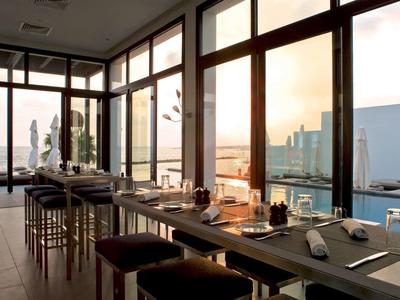 Modernes Restaurant mit großen Glasfenstern und Blick auf den Hafen bei Sonnenuntergang.