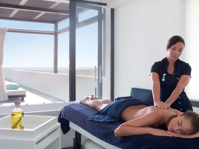 Eine Frau erhält Rückenmassage in hellem Raum mit Blick auf Meer und Terrasse.