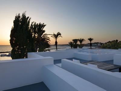 Terrasse mit weißen Wänden und Palmen bei Sonnenuntergang am Meer.