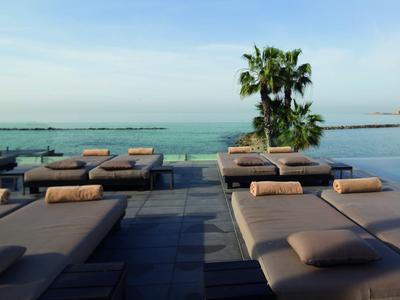 Elegantes camastros con cojines junto a la piscina con vista al mar y una palmera.
