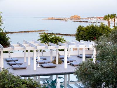 Moderner Hotelpoolbereich mit weißen Pergolen, Liegen und Blick aufs Meer und Hafen.