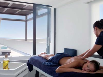 Frau erhält Rückenmassage in hellem Raum mit Blick auf Terrasse und Meer.