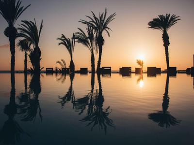 Pool mit Palmen und Sonnenuntergang im Hintergrund, ruhige Wasserreflexion sichtbar.