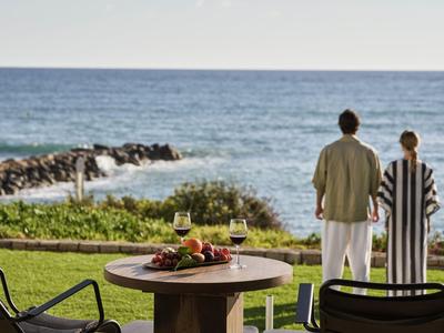 Ein Paar steht auf einer Grünfläche und schaut aufs Meer, im Vordergrund ein Tisch mit Essen und Getränken.