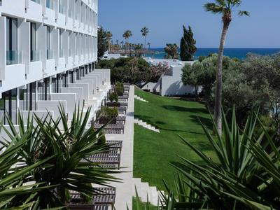 Blick auf die Terrasse eines Hotels mit Grünflächen und Meer im Hintergrund.