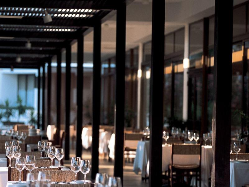 Modernes Restaurant mit gedeckten Tischen, weißen Tischdecken und Glasgeschirr unter Dachstruktur.