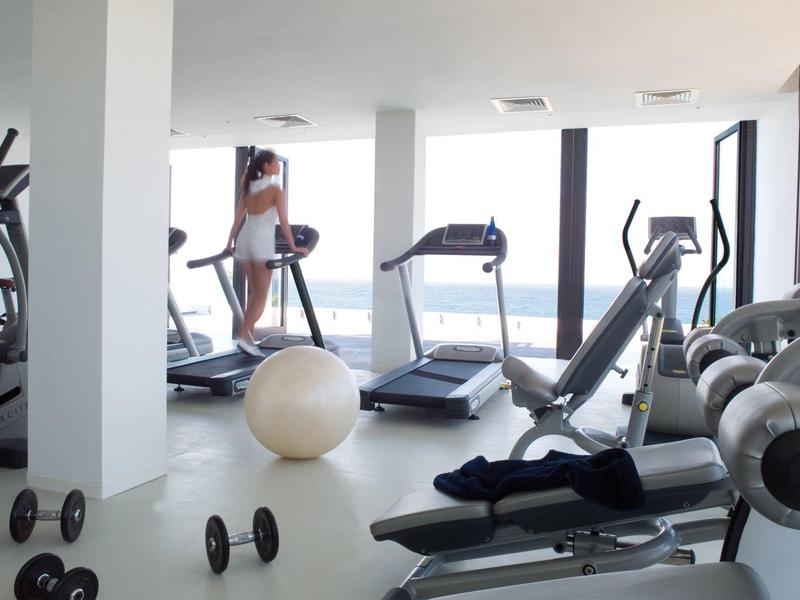 Moderner Fitnessraum mit Laufbändern, Hanteln, Gymnastikball und großen Fenstern mit Ausblick.