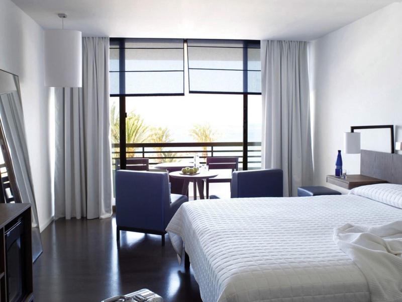 Modernes Schlafzimmer mit großem Fenster, zwei Sesseln, weißem Bett und dunklem Holzboden.