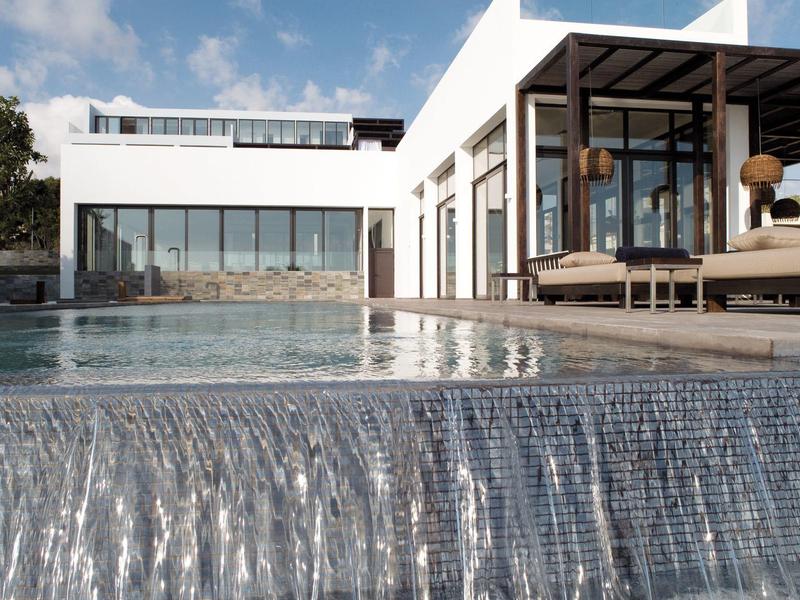 Moderner weißer Gebäudekomplex mit großem Glasfenster und Infinity-Pool mit Wasserfallkante.