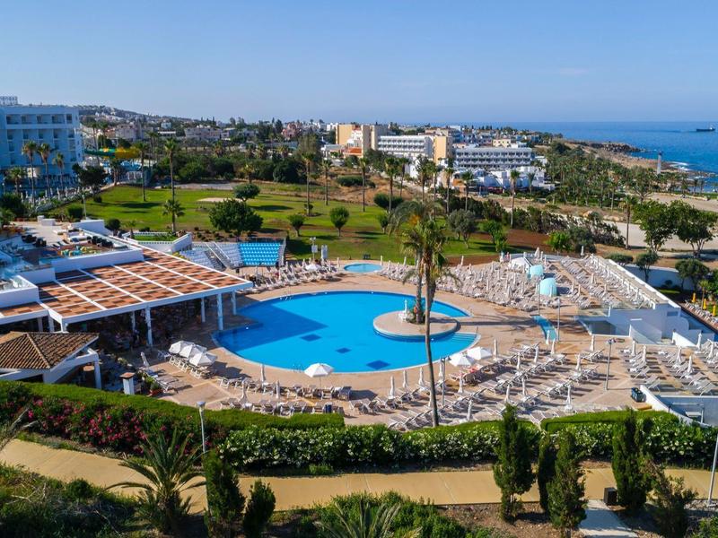 Große Poolanlage mit Liegestühlen, Palmen und mehreren Hotelgebäuden an der Küste.