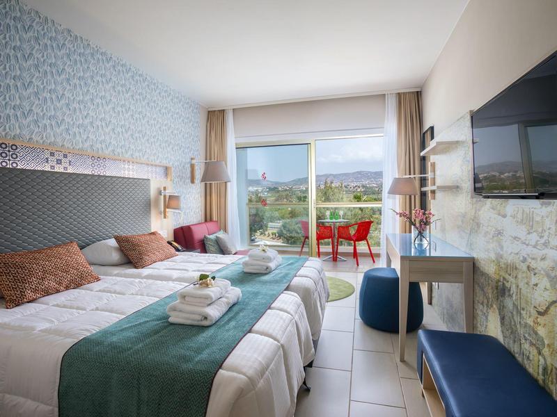 Hell eingerichtetes Schlafzimmer mit zwei Einzelbetten, Balkon und Blick auf grüne Landschaft.