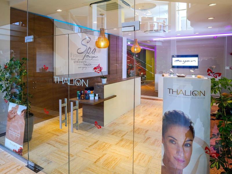 Moderner Wellnessbereich mit Glaswänden, hellen Holzböden, Pflanzen und Werbetafel.