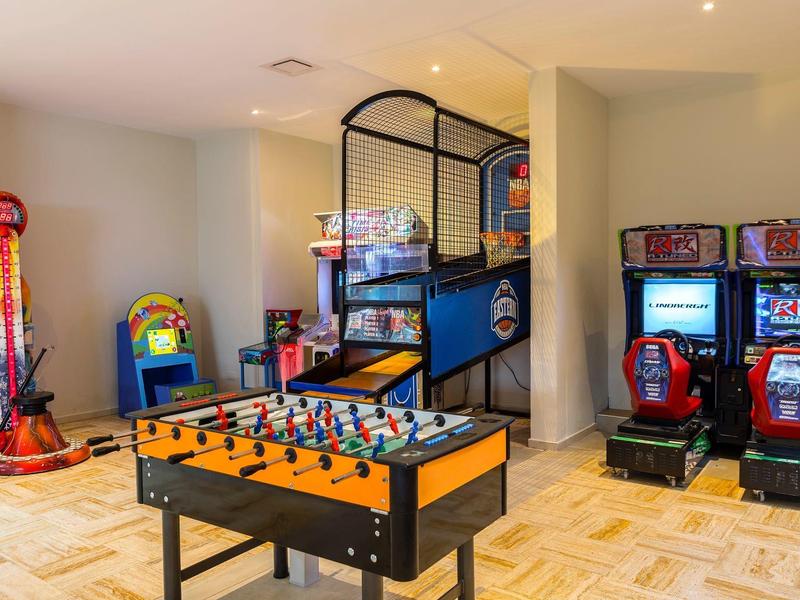 Spielezimmer mit Kicker, Basketballwurf, Rennspielen und Greifautomaten, helle Wände und Holzboden.