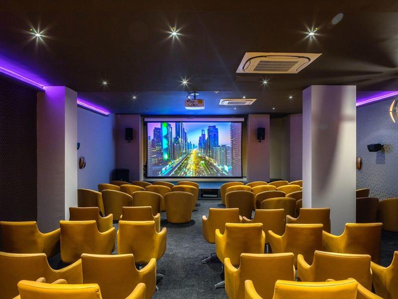 Kleiner Kinosaal mit gelben Sitzreihen, beleuchtet von lila LED-Leuchten und einer Filmleinwand vorne.