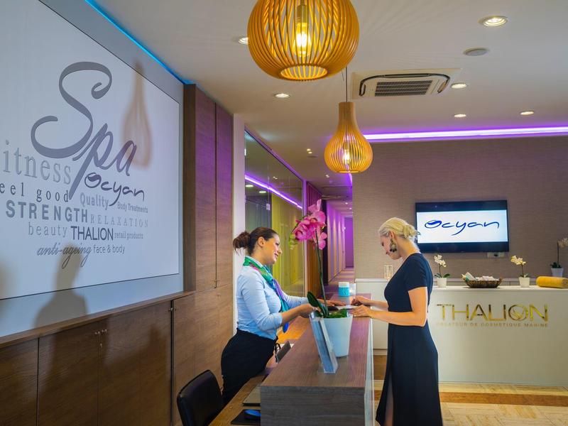 Innenraum eines Empfangsbereichs mit zwei Frauen am Empfangstresen, moderner Beleuchtung und Schildern.