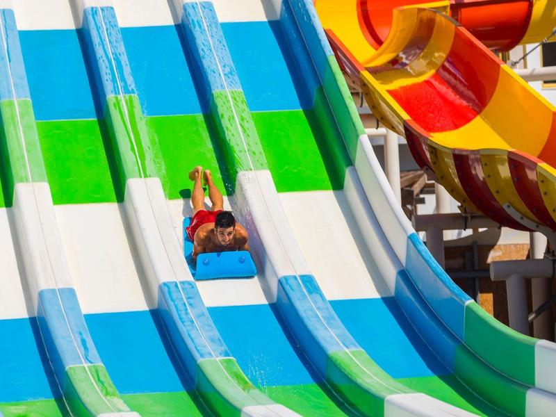 Mehrspurige Rutsche mit blau-grünen Streifen und zwei Personen, die nach unten rutschen.