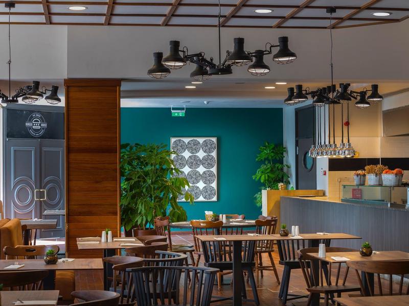 Modern eingerichtetes Café mit Holztischen, Stühlen, grünen Pflanzen und Hängelampen.