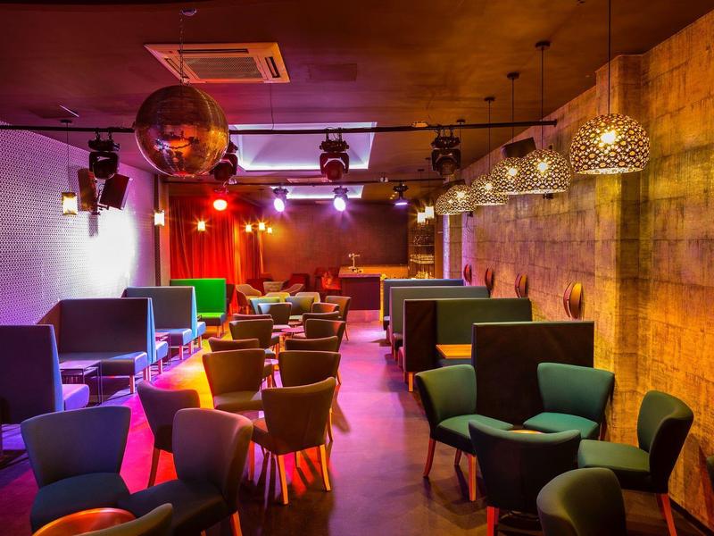 Moderner Loungebereich mit farbigen Sesseln, gedämpfter Beleuchtung und Betonwänden.