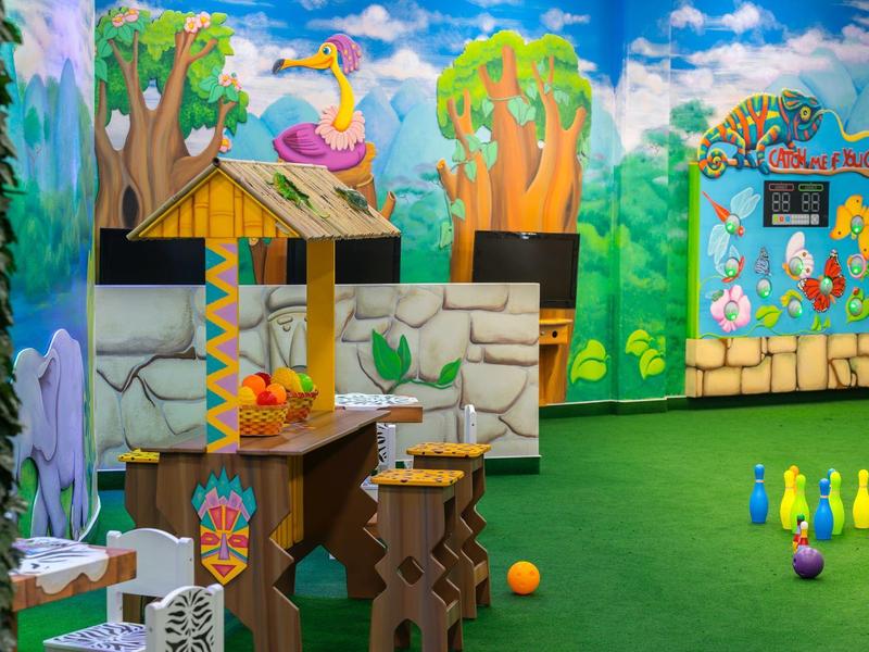 Bunter Indoor-Spielplatz mit Tiermotiven, Hütten, Kegeln und grünem Teppichboden.