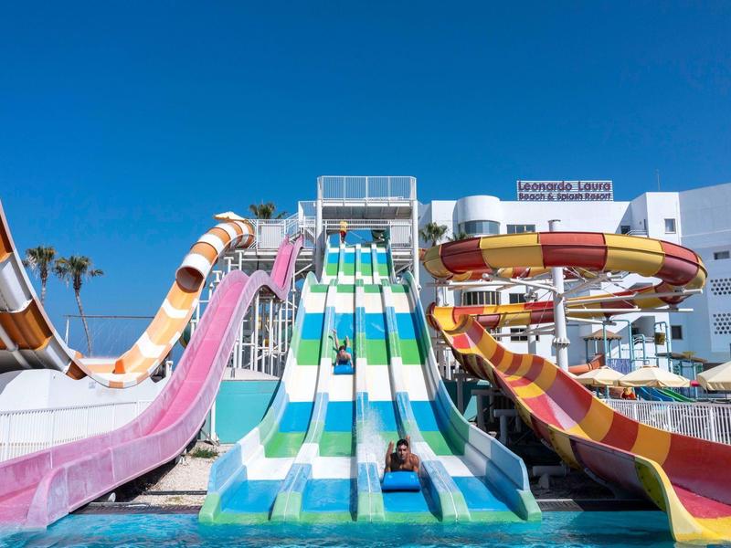 Bunte Wasserrutschen in verschiedenen Formen führen in ein klares Schwimmbecken unter blauem Himmel.