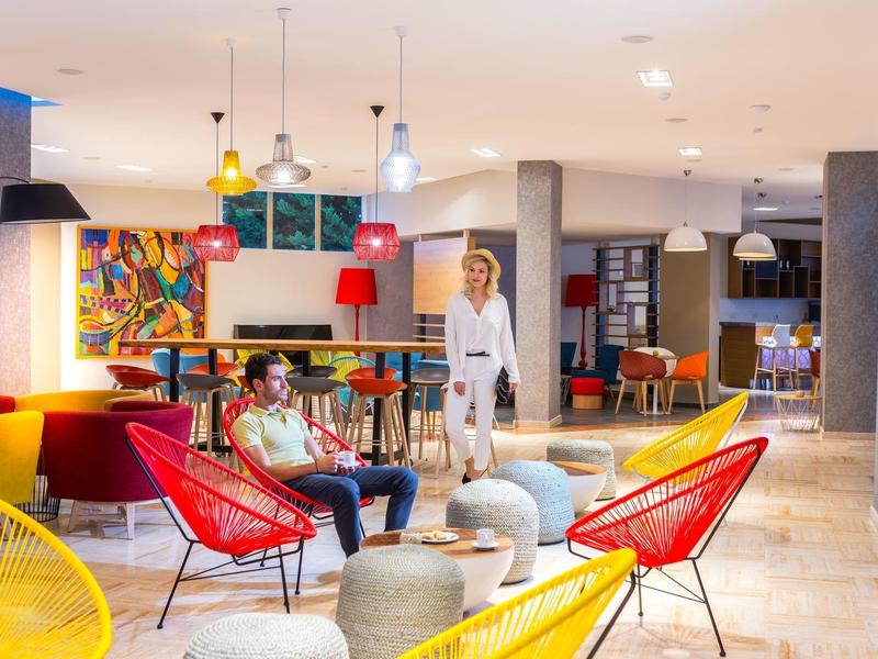 Moderner, heller Arbeitsraum mit bunten Stühlen, Sofas und zwei Personen im Gespräch.