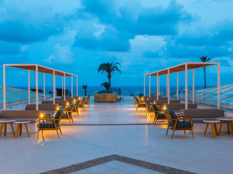 Luxuriöse Terrasse mit Liegen, Beleuchtung und Meerblick bei blauem Himmel und Wolken.