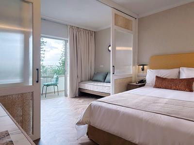 Camera d'hotel moderna con letto matrimoniale, divano e balcone con sedie e tavolo.