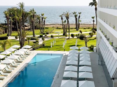 Área de piscina moderna con tumbonas y sombrillas, vista al mar y palmeras.