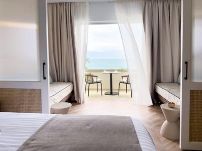 Heller Hotelbalkon mit Sitzbereich und Blick auf das Meer an einem sonnigen Tag.