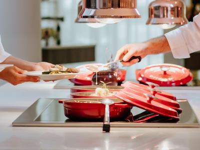 Kochaktivität mit roten Töpfen auf einem Herd und zwei Personen, die Essen servieren.