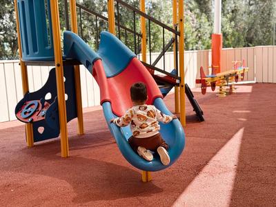 Niño deslizándose por un tobogán azul en un parque con suelo arenoso.