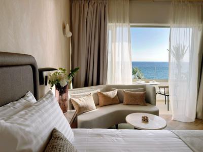 Gemütliche Hotelzimmersitzecke mit Panoramablick aufs Meer durch große Fenster.