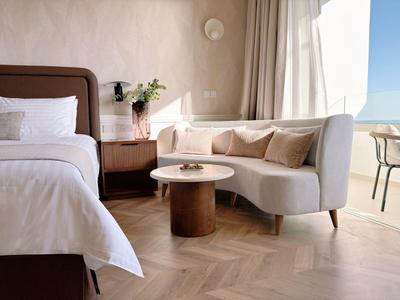 Elegantes Hotelzimmer mit Doppelbett, Sofa, Beistelltisch und Terrasse mit Meerblick.