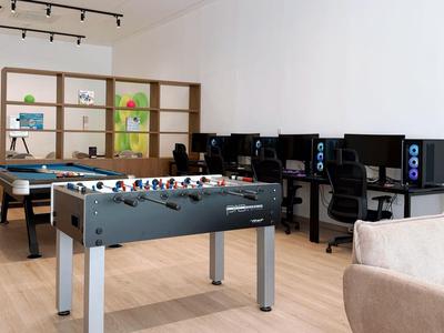 Sala de recreo moderna con futbolín, ping pong y varios ordenadores en un espacio luminoso.