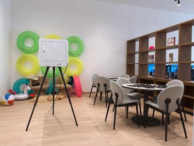 Área de salón moderna en hotel con sillas, mesas y flotadores coloridos en la pared.