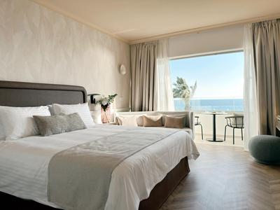 Schlafzimmer mit Doppelbett und Balkon mit Meerblick in einem Hotelzimmer.