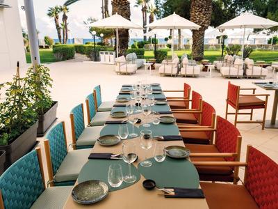 Langer Tisch mit bunten Stühlen und gedecktem Platz im Außenbereich eines Hotels.