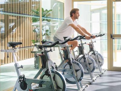 Moderner Fitnessraum mit mehreren stationären Fahrrädern vor großen Fenstern in einem Hotel.
