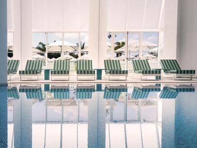 Reihe von grünen Liegestühlen entlang eines Innenpools mit großen Fenstern und Meeresblick.