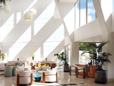 Helles Hotellobby mit moderner Einrichtung und großen Fenstern, die Tageslicht hereinlassen.