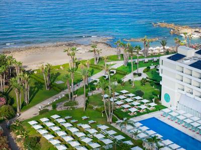 Hotelanlage mit Pool, Liegen auf Rasen und Meeresblick im Hintergrund.