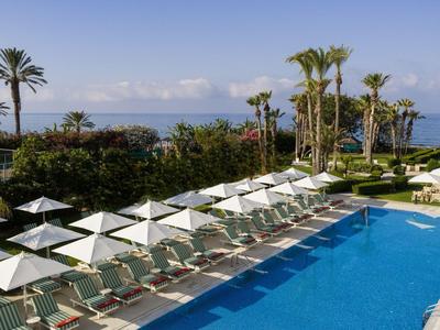 Großer Pool mit weißen Liegestühlen und Sonnenschirmen an tropischem Hotelstrand.