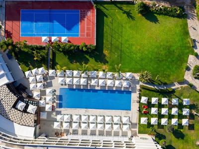 Vogelperspektive auf Hotelpool mit Liegestühlen und Tennisplatz im Grünen.