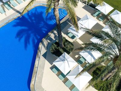 Blick von oben auf einen Pool mit blauer Wasserfläche, umgeben von Sonnenschirmen und Liegen.