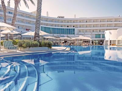 Großer Hotelpool mit Stufen, Sonnenschirmen und modernen Gebäuden im Hintergrund.