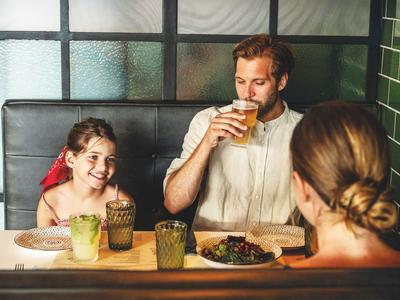Familie sitzt in Hotelrestaurant, Vater trinkt Bier, Tochter lacht, Mutter ist zu sehen.